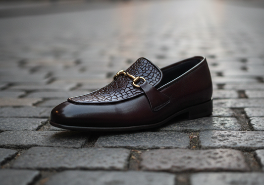Brown leather loafer with gold buckle on a cobblestone street